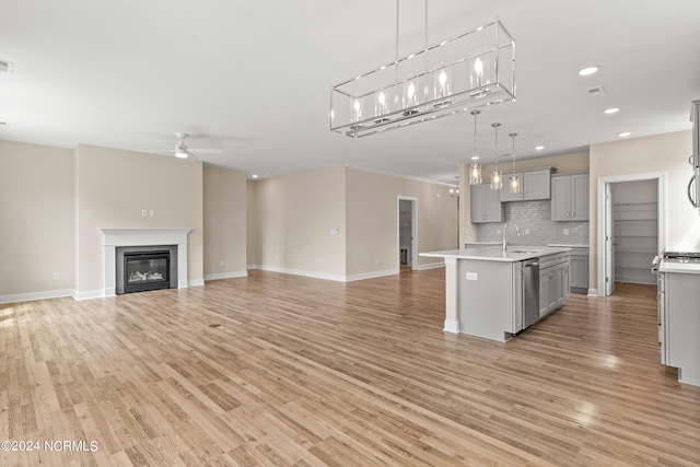 kitchen with open floor plan, a center island with sink, light countertops, gray cabinets, and a ceiling fan