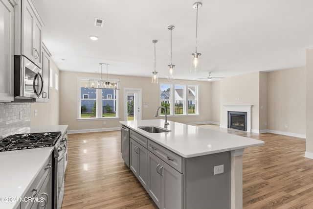 kitchen featuring gray cabinets, a sink, tasteful backsplash, appliances with stainless steel finishes, and a fireplace