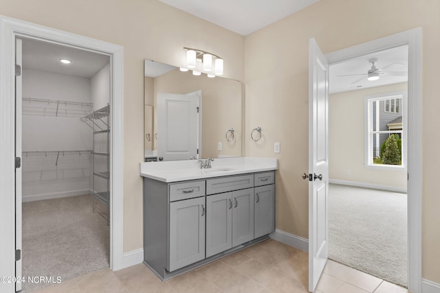 bathroom with vanity, baseboards, ceiling fan, a walk in closet, and tile patterned floors