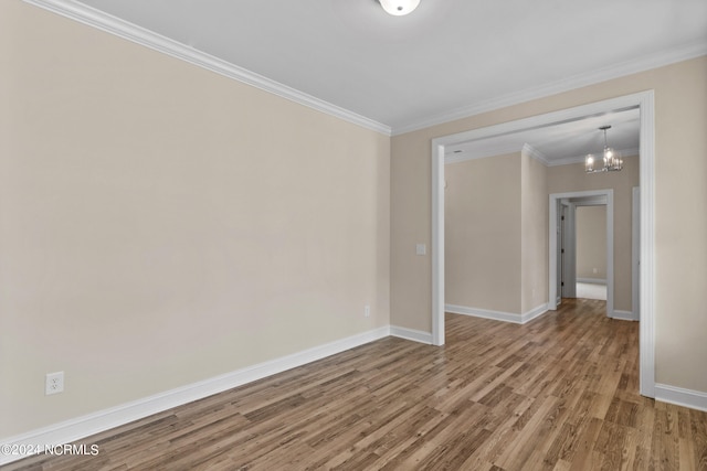 empty room featuring a notable chandelier, wood finished floors, baseboards, and ornamental molding