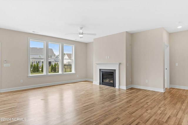 unfurnished living room featuring baseboards, light wood-style floors, a glass covered fireplace, and a ceiling fan