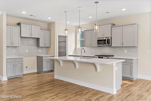 kitchen with gray cabinetry, a kitchen island with sink, a sink, stainless steel microwave, and a kitchen breakfast bar