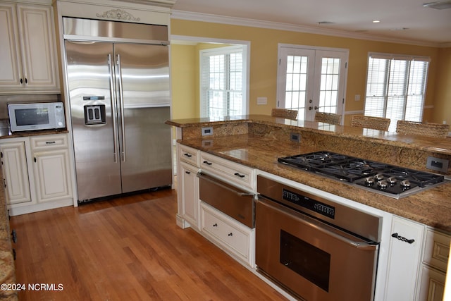 kitchen featuring french doors, light wood-type flooring, dark stone counters, stainless steel appliances, and crown molding