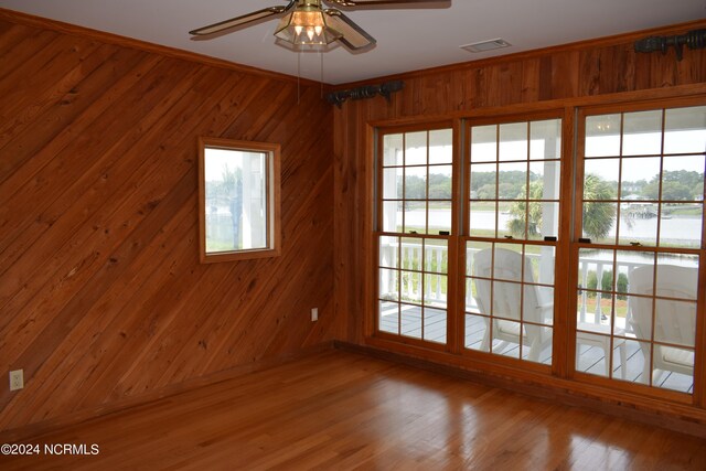 spare room featuring hardwood / wood-style flooring, ceiling fan, ornamental molding, and wooden walls