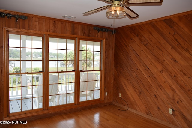 empty room with hardwood / wood-style flooring, ceiling fan, and wood walls