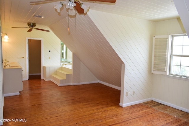 additional living space featuring ceiling fan, light hardwood / wood-style flooring, vaulted ceiling, and wooden walls