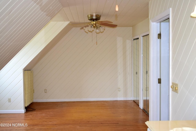 additional living space with wooden walls, hardwood / wood-style floors, and ceiling fan