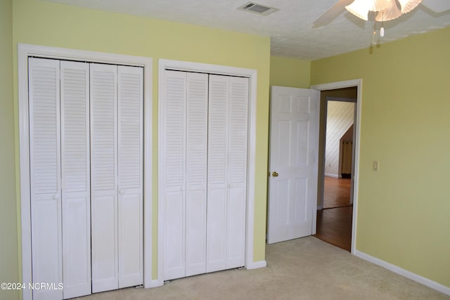 unfurnished bedroom with ceiling fan, light carpet, and two closets