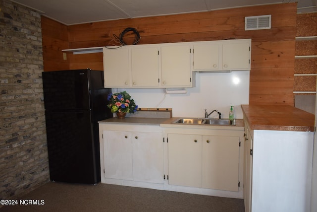 kitchen featuring white cabinetry, black fridge, sink, and wood walls