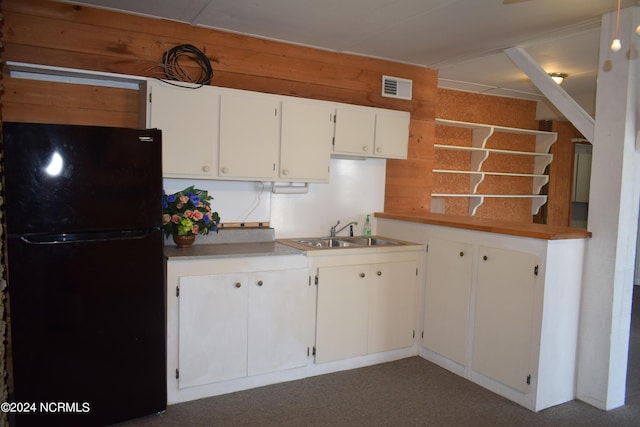 kitchen with sink, black fridge, wood walls, white cabinets, and dark carpet