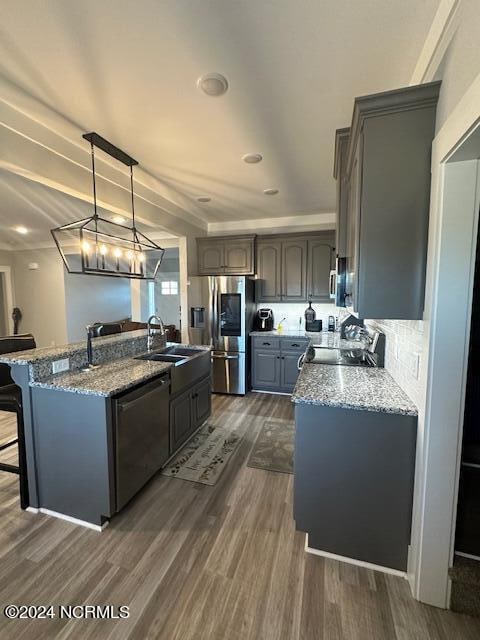 kitchen with stainless steel appliances, pendant lighting, dark hardwood / wood-style flooring, and light stone counters