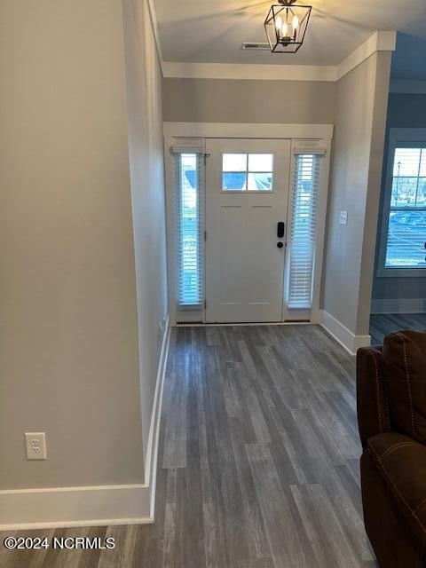 foyer entrance with dark wood-type flooring, crown molding, and a chandelier