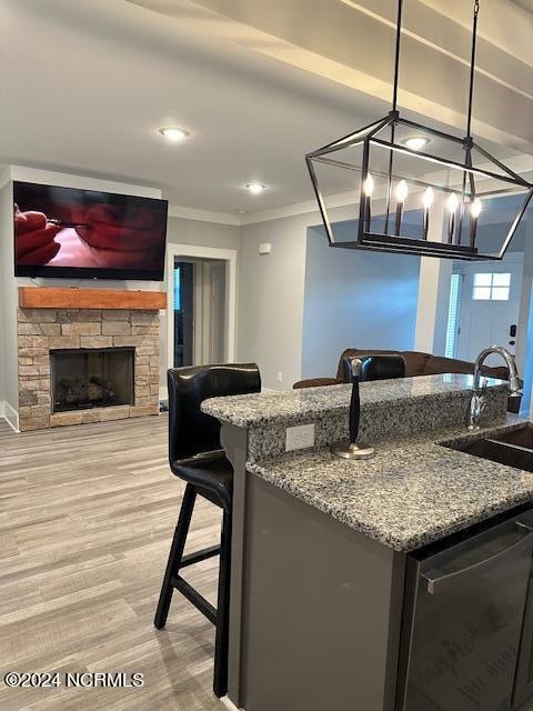 kitchen with a fireplace, ornamental molding, dark stone counters, light hardwood / wood-style floors, and dishwasher