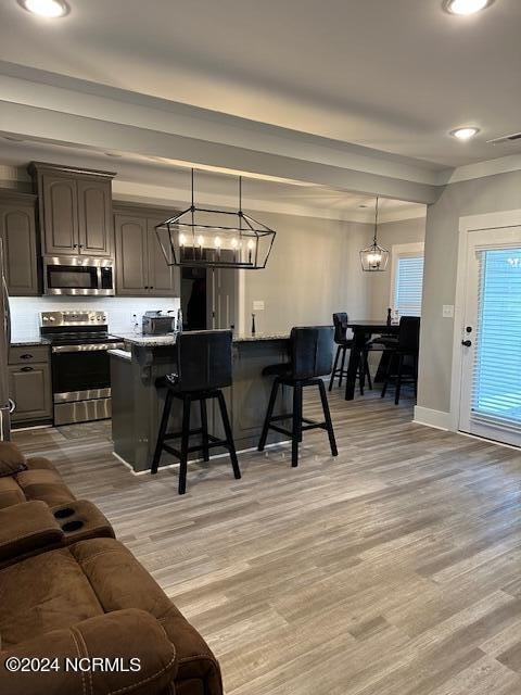 kitchen with light hardwood / wood-style floors, a breakfast bar area, decorative light fixtures, stainless steel appliances, and an inviting chandelier