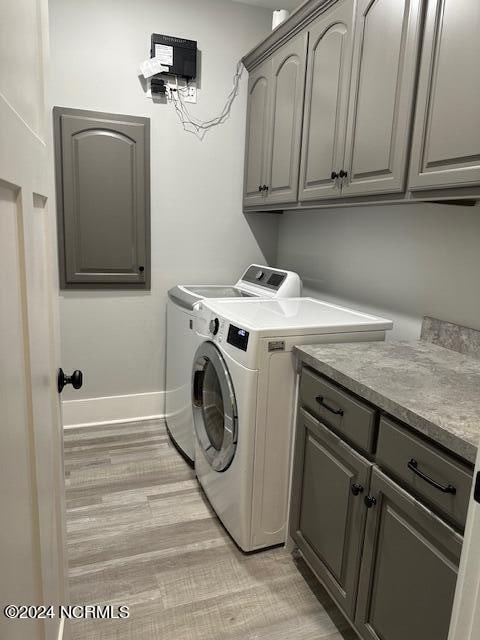 laundry room with washing machine and clothes dryer, cabinets, and light wood-type flooring