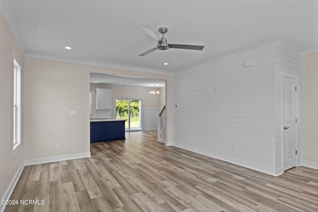 unfurnished living room with ceiling fan with notable chandelier, light hardwood / wood-style floors, and ornamental molding