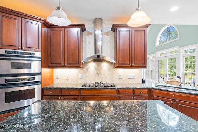 kitchen with wall chimney range hood, dark stone counters, tasteful backsplash, and appliances with stainless steel finishes