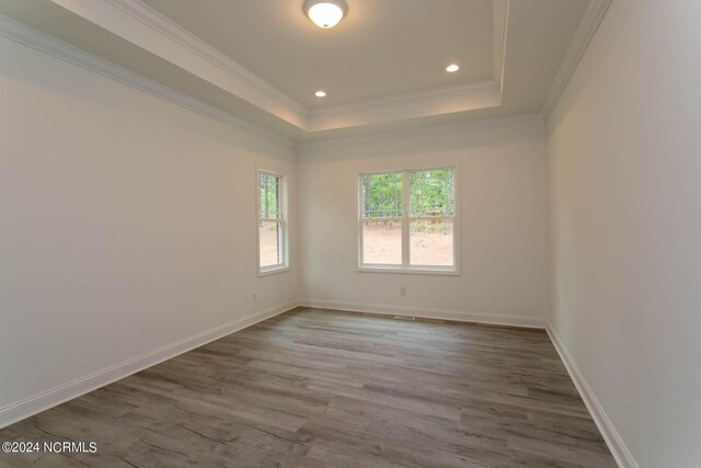 empty room with hardwood / wood-style flooring, a raised ceiling, and crown molding