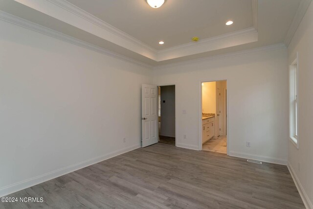 unfurnished bedroom featuring ornamental molding, hardwood / wood-style floors, connected bathroom, and a raised ceiling