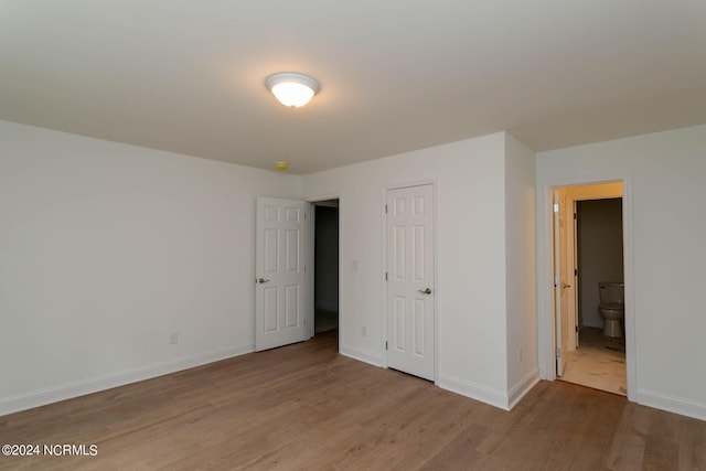 unfurnished bedroom with a closet, wood-type flooring, and connected bathroom