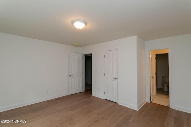 unfurnished bedroom featuring ensuite bathroom, wood finished floors, and baseboards