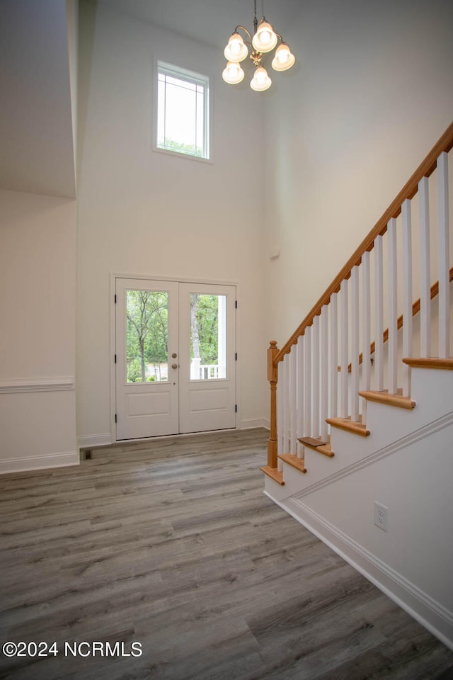 foyer with a towering ceiling, french doors, hardwood / wood-style flooring, and a chandelier