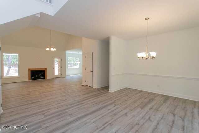 unfurnished living room with high vaulted ceiling, an inviting chandelier, and light hardwood / wood-style flooring