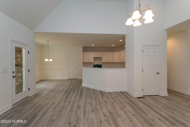 unfurnished living room featuring high vaulted ceiling, hanging light fixtures, and light wood-type flooring