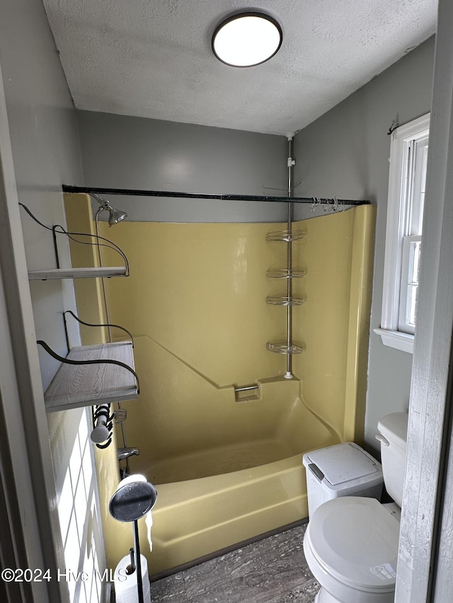 bathroom featuring washtub / shower combination, toilet, wood-type flooring, and a textured ceiling