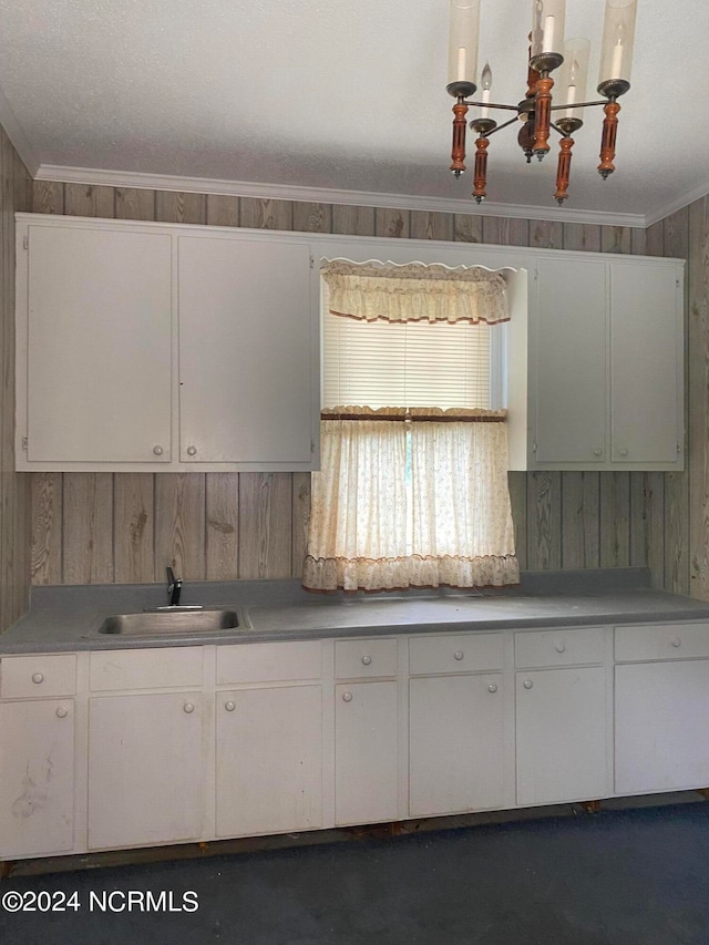 kitchen featuring ornamental molding, wood walls, white cabinetry, and sink