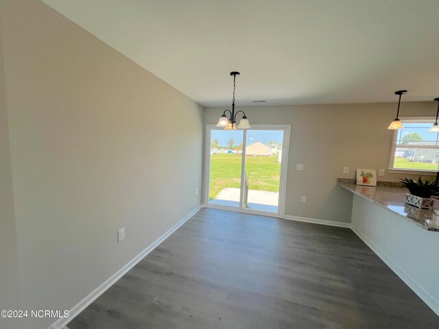 unfurnished dining area with a chandelier, dark wood-type flooring, and baseboards