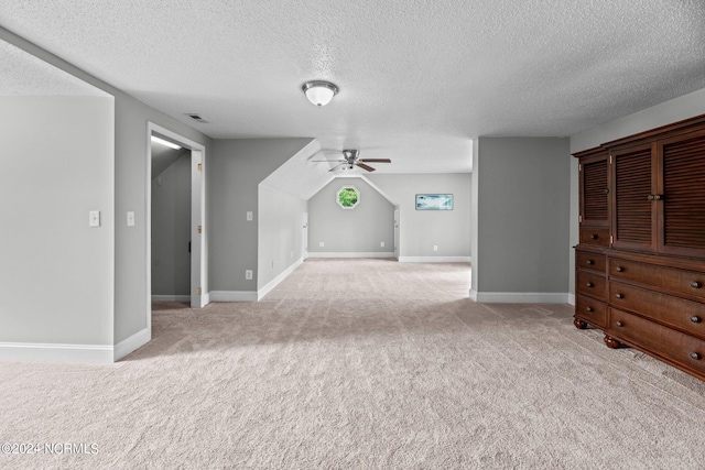 interior space with a textured ceiling, ceiling fan, and light colored carpet