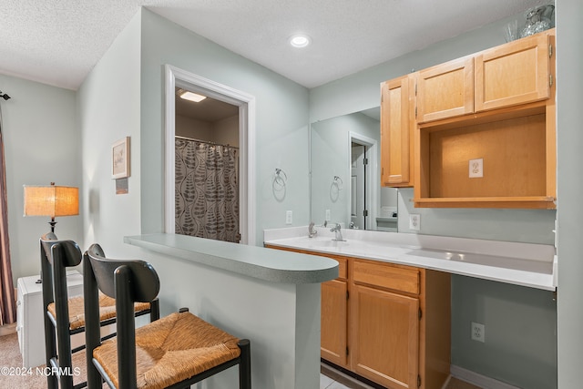 kitchen with kitchen peninsula, a textured ceiling, a kitchen bar, and light brown cabinetry