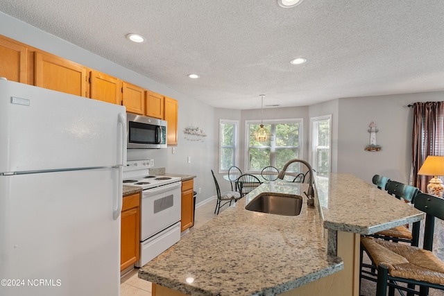 kitchen with white appliances, a kitchen island with sink, decorative light fixtures, sink, and light tile floors