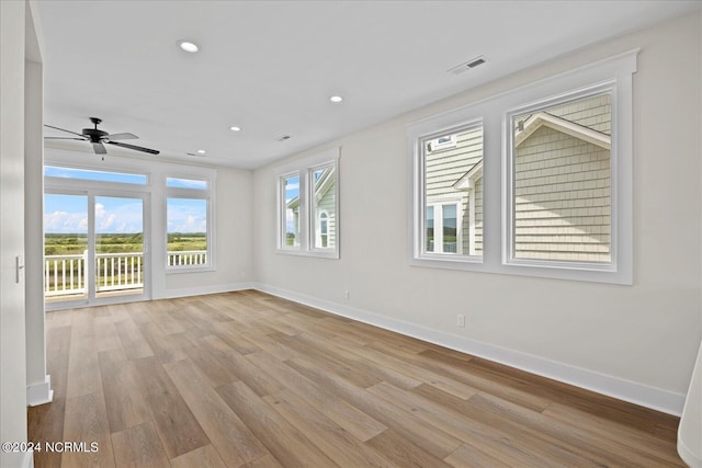 empty room with a wealth of natural light, light wood-type flooring, visible vents, and baseboards