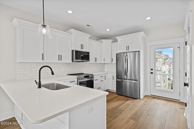 kitchen featuring white cabinets, appliances with stainless steel finishes, light countertops, pendant lighting, and a sink