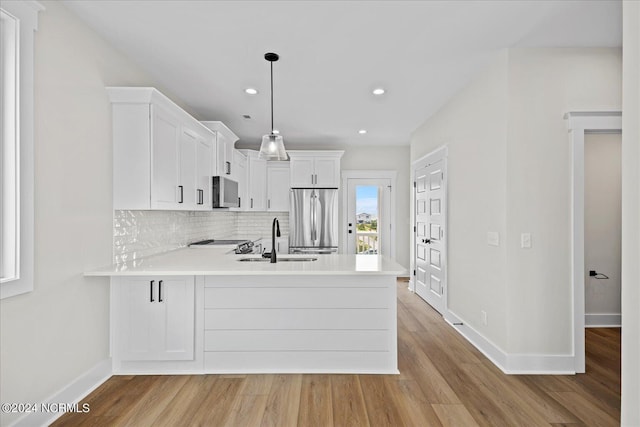 kitchen featuring a peninsula, stainless steel appliances, a sink, white cabinetry, and light countertops