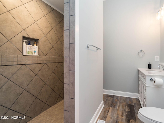 bathroom with hardwood / wood-style floors, vanity, crown molding, toilet, and tiled shower