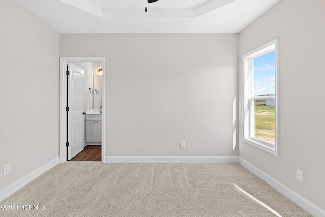 unfurnished bedroom with dark colored carpet, ensuite bath, multiple windows, and a raised ceiling