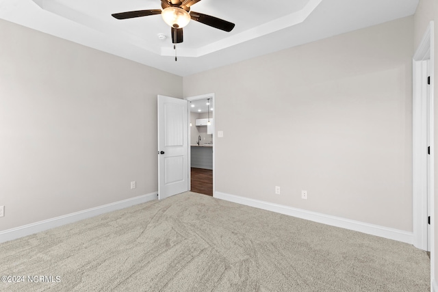 empty room with carpet, ceiling fan, a raised ceiling, and sink