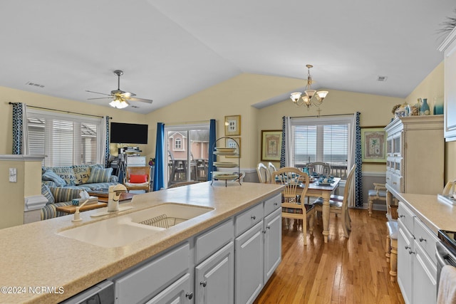 kitchen with lofted ceiling, ceiling fan with notable chandelier, sink, hanging light fixtures, and light hardwood / wood-style floors