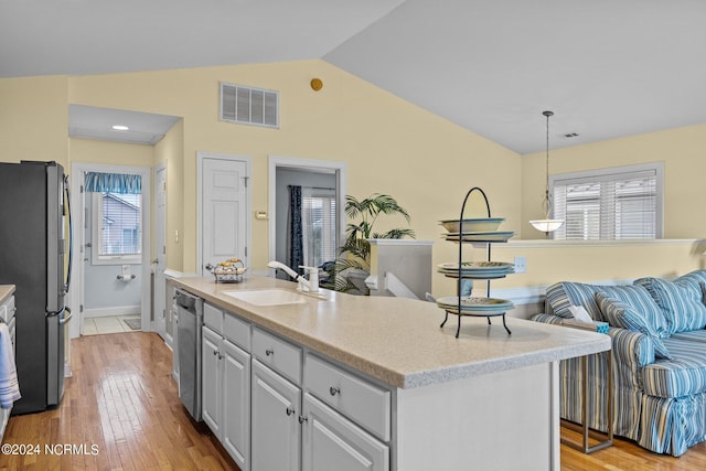 kitchen featuring appliances with stainless steel finishes, sink, pendant lighting, light hardwood / wood-style floors, and an island with sink