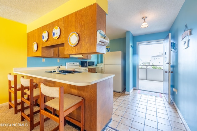 kitchen with a textured ceiling, kitchen peninsula, white appliances, and a kitchen bar