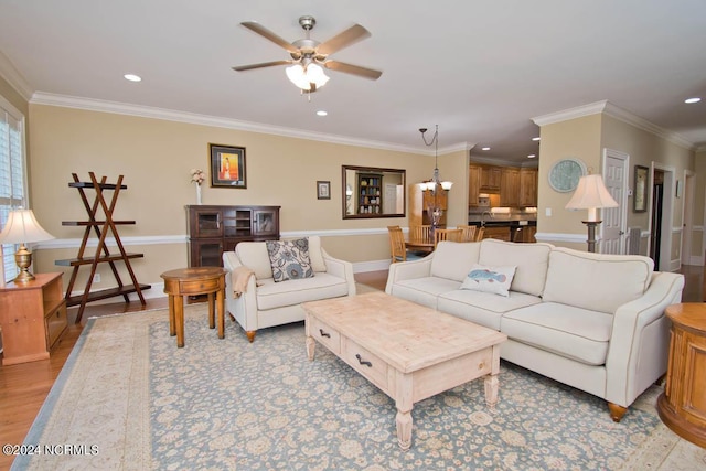 living room with ornamental molding, ceiling fan with notable chandelier, and light hardwood / wood-style floors