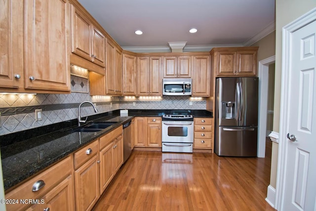 kitchen with sink, wood-type flooring, ornamental molding, appliances with stainless steel finishes, and dark stone counters