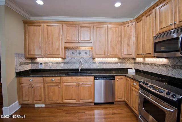 kitchen with sink, appliances with stainless steel finishes, ornamental molding, dark hardwood / wood-style flooring, and dark stone counters