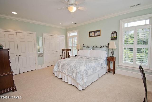 carpeted bedroom with multiple windows, crown molding, ceiling fan, and two closets