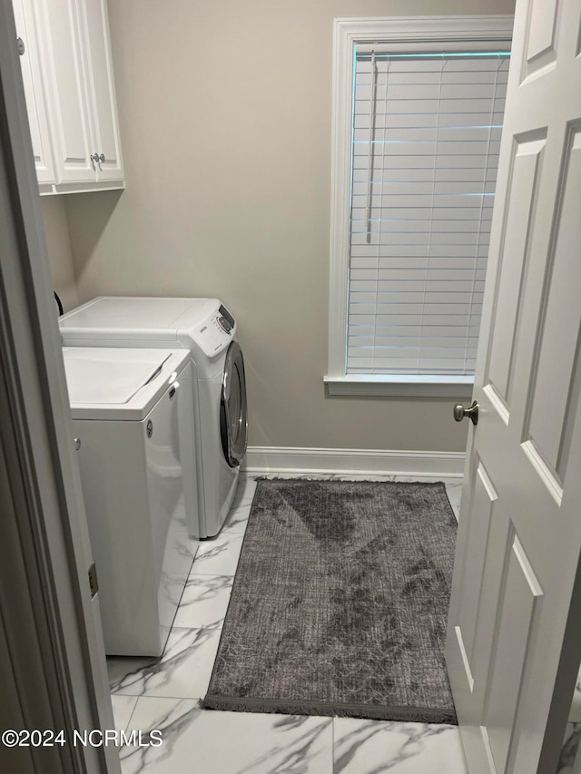 clothes washing area featuring separate washer and dryer, light tile floors, and cabinets