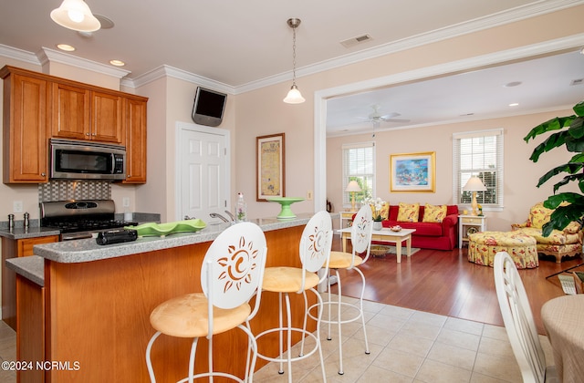 kitchen with stainless steel appliances, hanging light fixtures, crown molding, a kitchen bar, and light tile floors