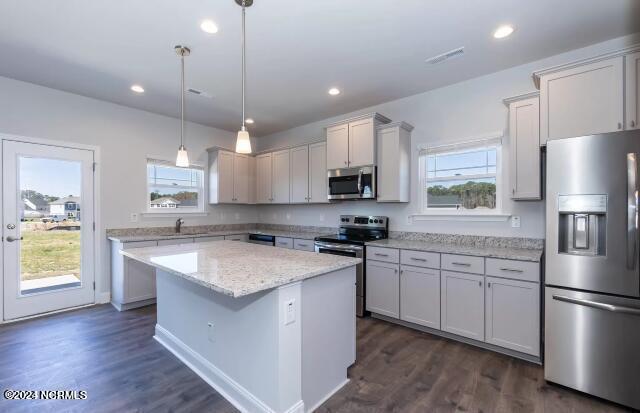 kitchen featuring a kitchen island, appliances with stainless steel finishes, dark hardwood / wood-style flooring, hanging light fixtures, and light stone countertops